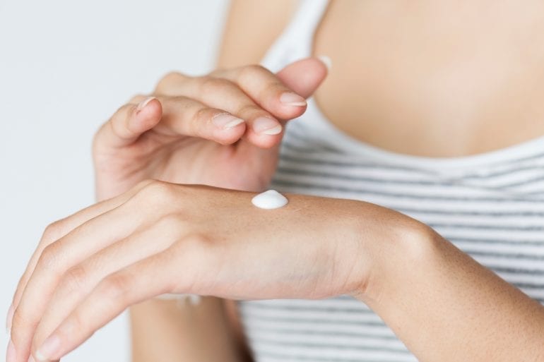 Image of a woman applying moisturizer to her hand for an anti-aging skincare routine.